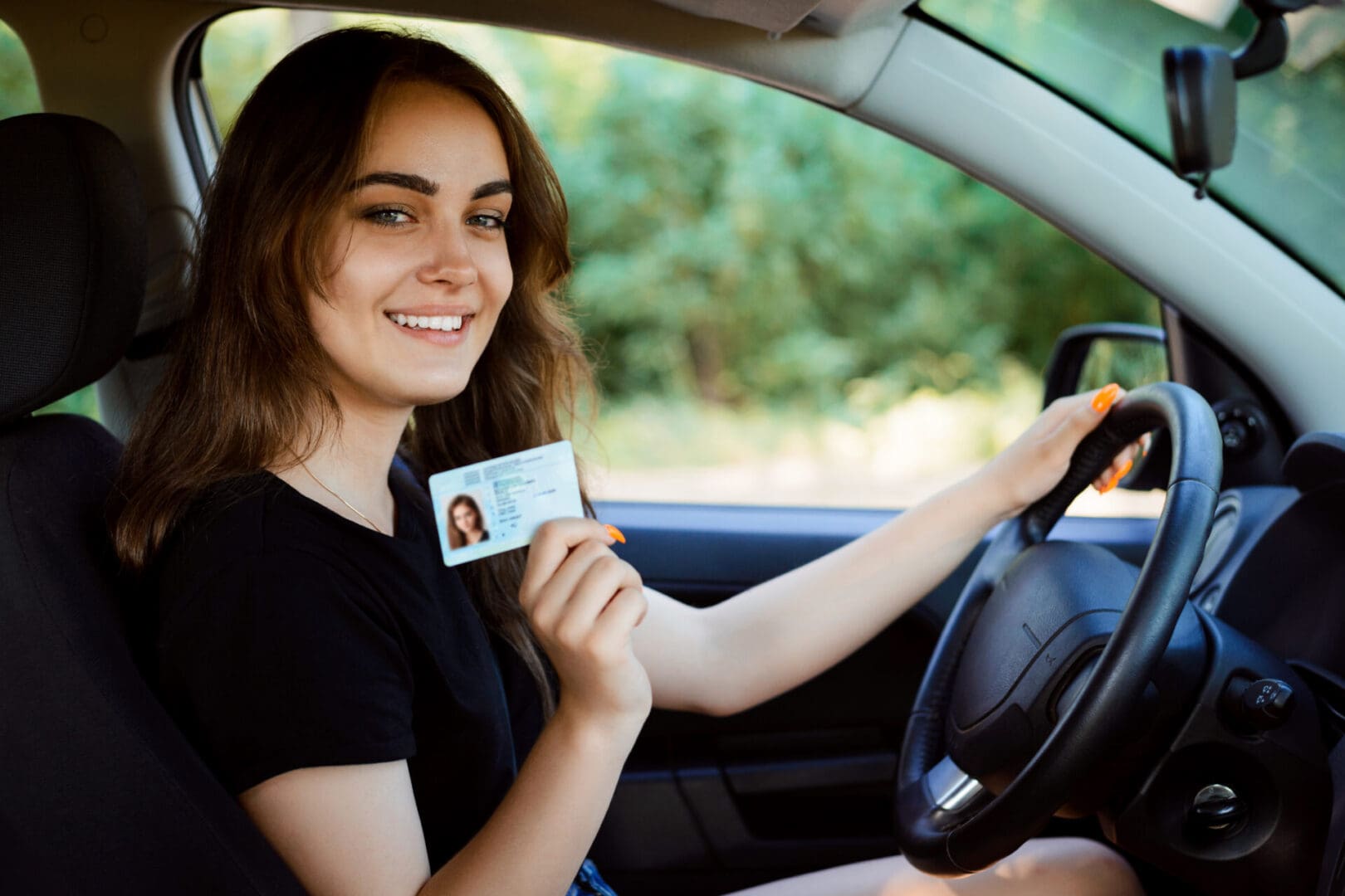 A woman holding up her driver 's license in the drivers seat of a car.